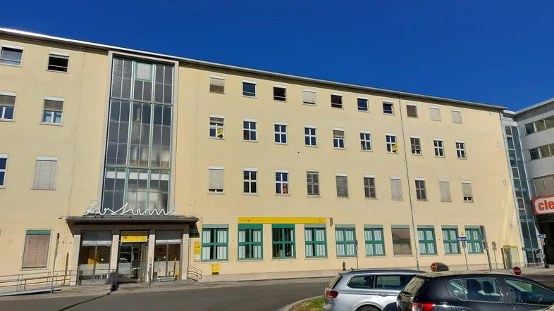 Großes, mehrstöckiges Gebäude mit vielen Fenstern und einer Rampe am Eingang unter blauem Himmel.