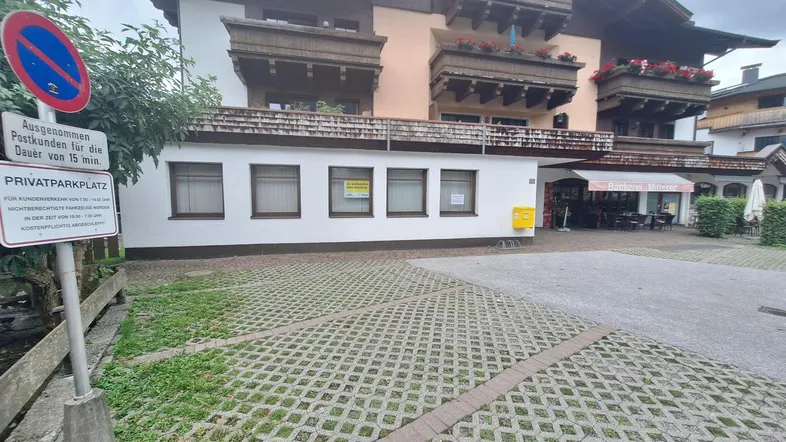 Außenansicht eines Gebäudes mit traditionellen Holzbalkonen und einem privaten Parkplatz im Vordergrund.
