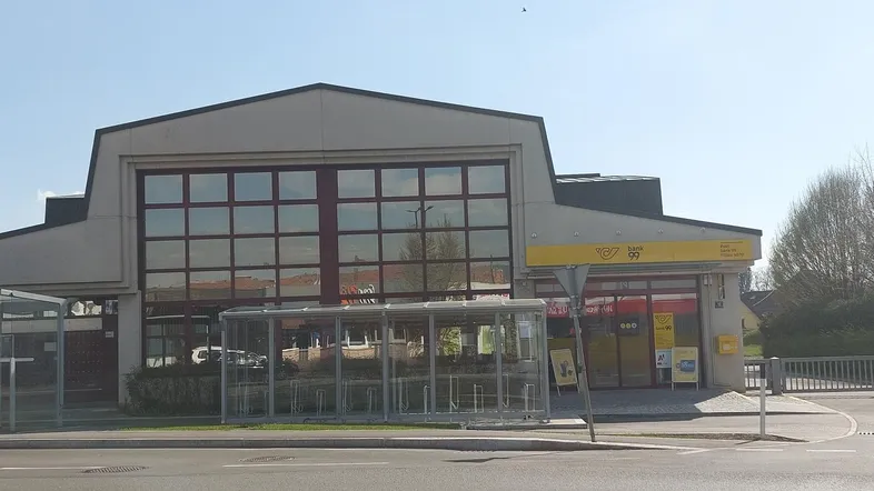 Außenansicht eines modernen Geschäftsgebäudes mit großen Fenstern und einer Postfiliale im Erdgeschoss.
