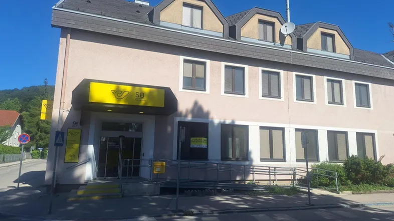 Fassade eines Gebäudes mit Post- und Bankfiliale, Rampe und mehreren Fenstern.
