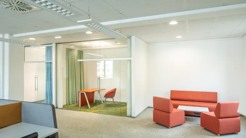 Moderner Großraumbüro mit Arbeitsplätzen, einer gläsernen Besprechungsbox und einer gemütlichen Lounge-Ecke.