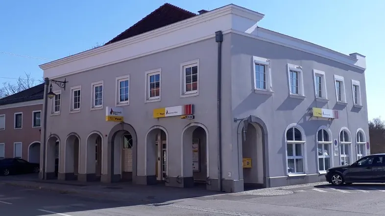 Historisches Gebäude mit grauer Fassade und Arkaden im Erdgeschoss, an einer Straße gelegen.