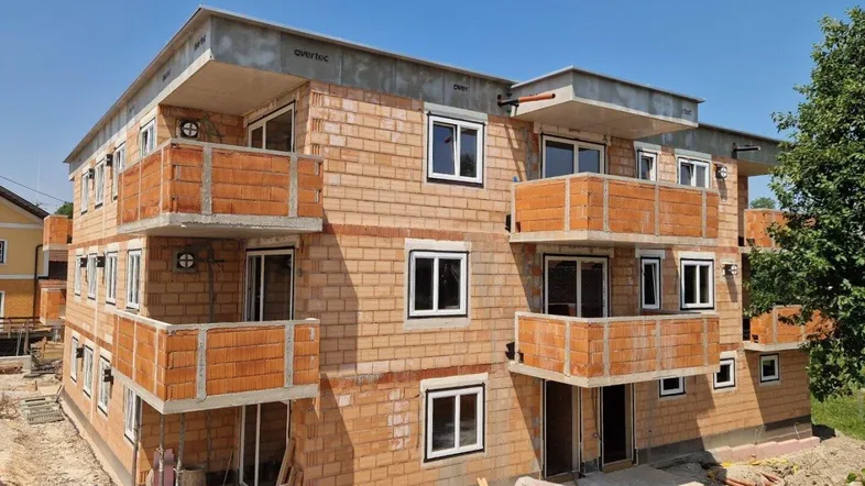 Neubau eines Mehrfamilienhauses in Rohbauweise mit sichtbaren Ziegelwänden und Balkonen.