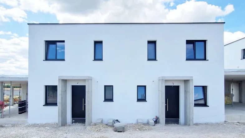 Moderne Doppelhaushälfte im Rohbauzustand mit weißer Fassade und schwarzen Fenstern.
