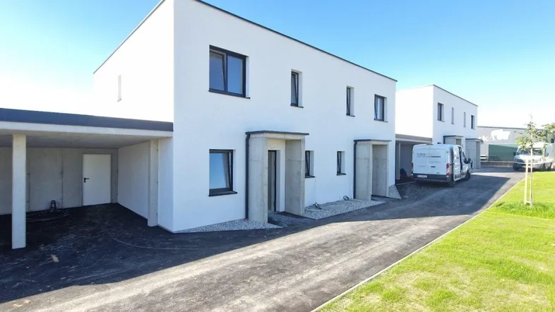 Moderne weiße Reihenhäuser mit klaren Linien und integrierten Carports, umgeben von Grünflächen und Zufahrten.