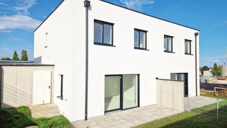 Modernes, weißes Reihenhaus mit Flachdach, kleiner Terrasse und Gartenbereich.