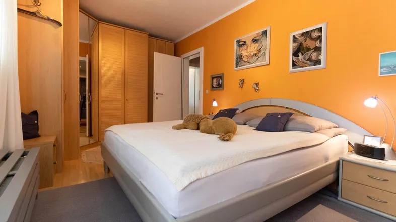 Helles Schlafzimmer mit orangefarbenen Wänden, Doppelbett und integrierten Holzschränken.