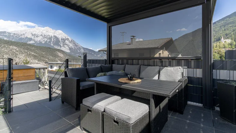 Moderne Terrasse mit bequemen Loungemöbeln, Esstisch und beeindruckendem Bergblick unter einer Pergola.