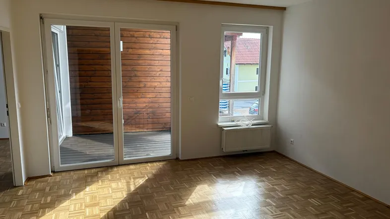 Helles Zimmer mit Parkettboden und Zugang zu einem Balkon, durchflutet von natürlichem Sonnenlicht.