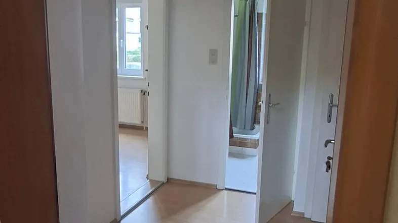 Blick durch einen Türrahmen in einen hellen Flur mit Holzfußboden und weiteren Türen.