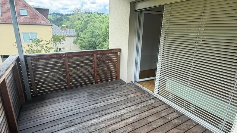 Überdachter Balkon mit Holzboden und Blick auf die umliegende Wohngegend und grüne Hügel.