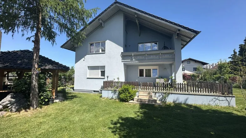 Hausfassade mit gepflegtem Garten, Rasenfläche und einer kleinen Terrasse.