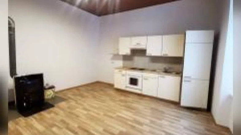 Geräumiger Raum mit einfacher Küchenzeile, Holzfußboden und einem Ofen für wohlige Wärme.