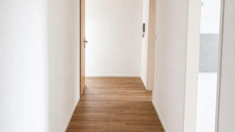 Heller Flur mit Laminatboden und weißen Wänden, der zu weiteren Räumen führt.