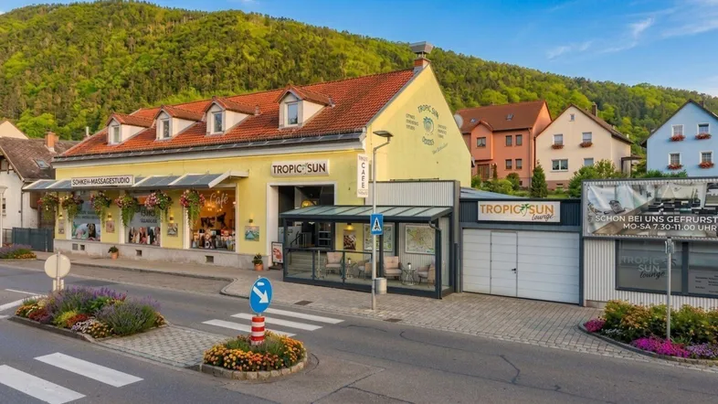 Ansicht des Gebäudes von der Straße mit Geschäften im Erdgeschoss und grünen Bergen im Hintergrund.