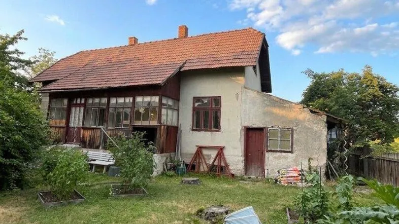 Altes Wohnhaus mit rotem Ziegeldach und verglaster Veranda, umgeben von einem naturnahen Garten mit Hochbeeten.