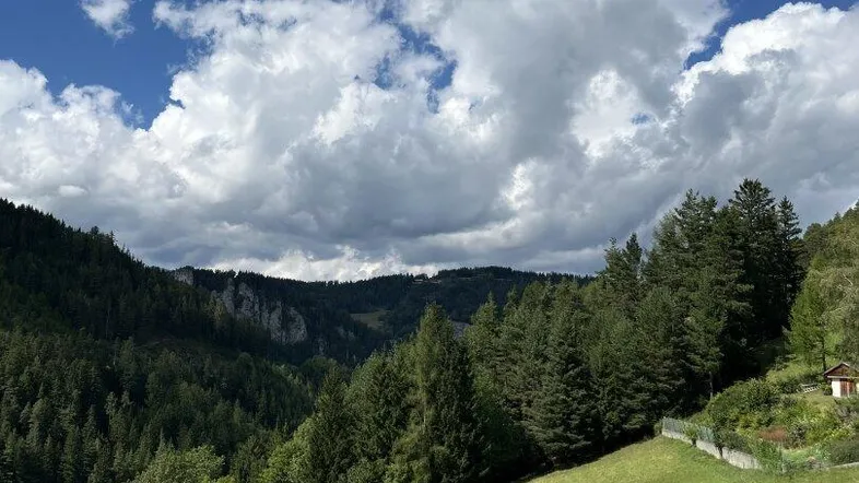 Malerische Landschaft mit grünen Hügeln, dichten Wäldern und einem weiten Himmel mit Wolken.