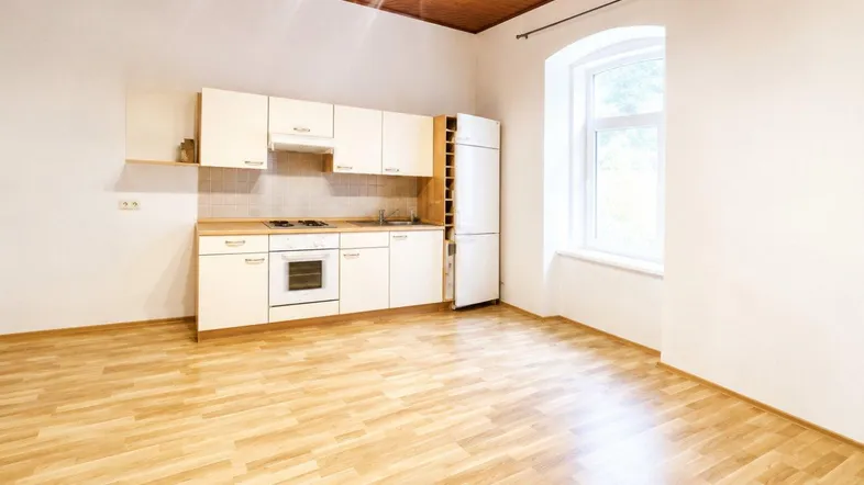 Heller Raum mit kleiner Einbauküche, Holzdecke und Laminatboden sowie einem Fenster.