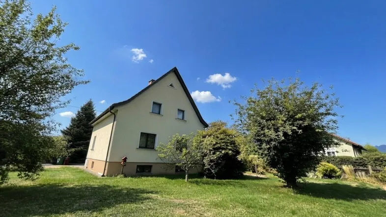 Freistehendes Einfamilienhaus mit großem Garten und gepflegter Rasenfläche unter blauem Himmel.