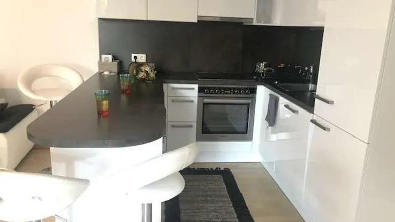 Moderne Küche mit weißen Hochglanzfronten, dunkler Arbeitsplatte und integrierter Frühstücksbar.