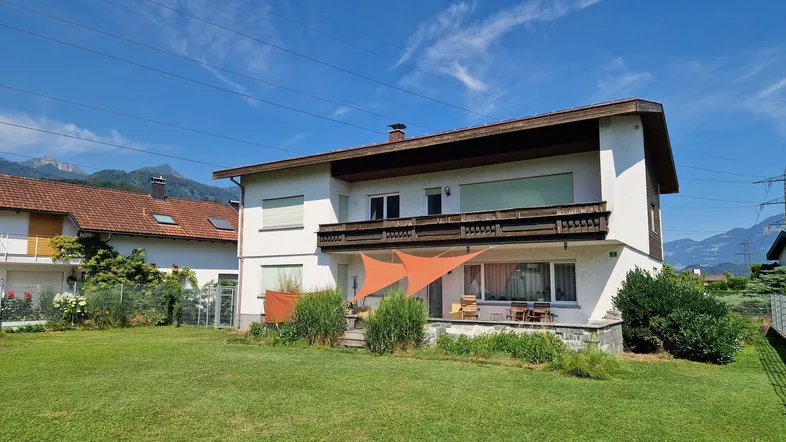 Großzügiger Gartenbereich mit Rasenfläche, Terrasse und Blick auf die umliegende Berglandschaft.