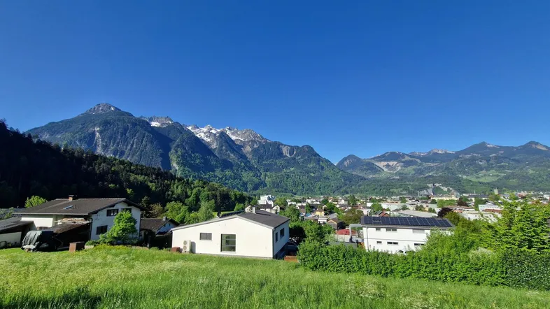 Panoramablick auf eine Wohnsiedlung mit majestätischen Bergen im Hintergrund unter blauem Himmel.
