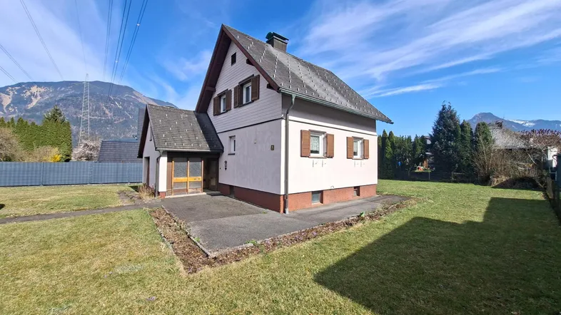 Freistehendes Einfamilienhaus mit großem Garten und Bergblick unter blauem Himmel.