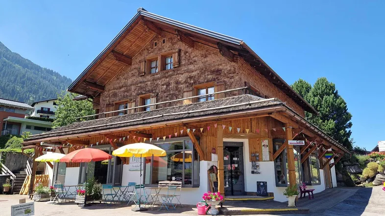 Traditionelles Holzhaus im Chalet-Stil mit Vordach und kleiner Außenterrasse unter Sonnenschirmen.