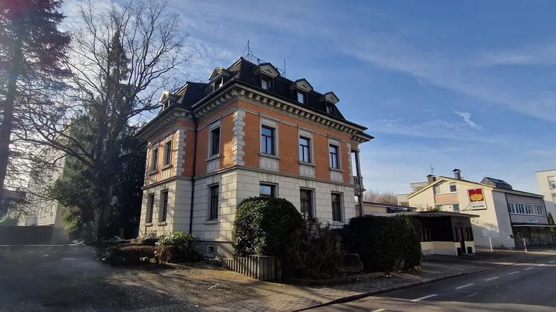 Historisches Gebäude mit Mansarddach und klassischer Fassade unter blauem Himmel.