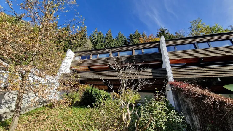 Modernes Gebäude mit Holzfassade, umgeben von Bäumen und Natur, unter blauem Himmel.