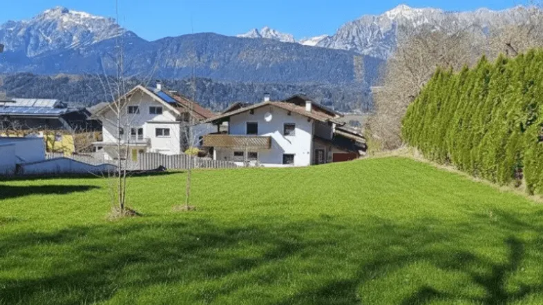 Grüne Rasenfläche mit Blick auf Wohnhäuser und die majestätische Berglandschaft unter blauem Himmel.