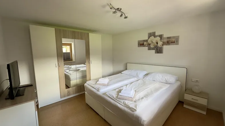 Helles Schlafzimmer mit Doppelbett, großem Kleiderschrank mit Spiegeltür und Korkboden.