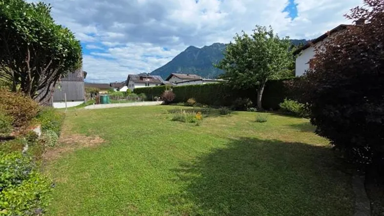 Gepflegter Gartenbereich mit Rasenfläche und Blick auf die umliegenden Berge unter blauem Himmel.