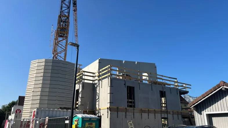 Baustelle eines Neubaus mit Kran und im Rohbau befindlichem Gebäude unter blauem Himmel.