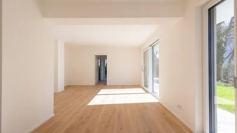 Heller, leerer Wohnraum mit großen Schiebetüren zum Garten und hellem Holzfußboden.