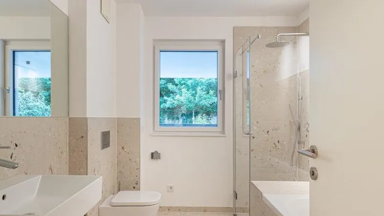Modernes Badezimmer mit Dusche, Badewanne, WC und Fenster mit Blick ins Grüne.