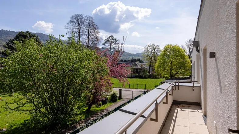 Heller Balkon mit Blick ins Grüne und auf die umliegende Landschaft unter blauem Himmel.