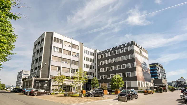 Modernes Bürogebäude im Technopark mit Parkplätzen und klarer Architektur unter blauem Himmel.
