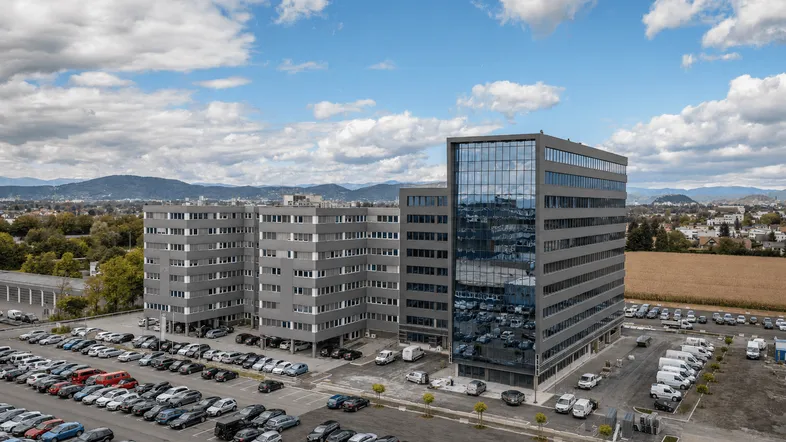 Luftaufnahme eines modernen Bürokomplexes mit mehreren Gebäuden und großem Parkplatz unter bewölktem Himmel.