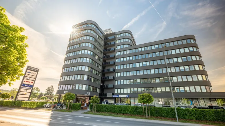 Modernes Bürogebäude mit geschwungener Fassade und viel Glas, umgeben von Grünflächen.