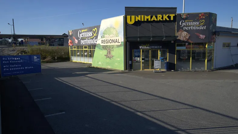 Vorderansicht des Supermarktes mit Werbeflächen und einem Teil des Parkplatzes.