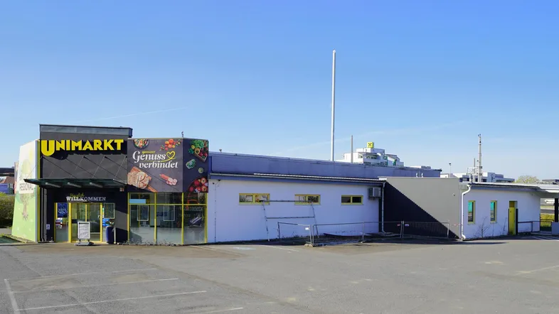 Außenansicht eines Supermarktes mit großem Parkplatz unter klarem blauem Himmel.