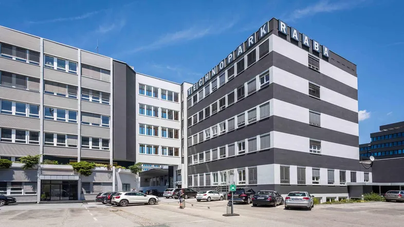 Modernes Bürogebäude mit markanter schwarz-weißer Fassade und Parkplätzen unter blauem Himmel.