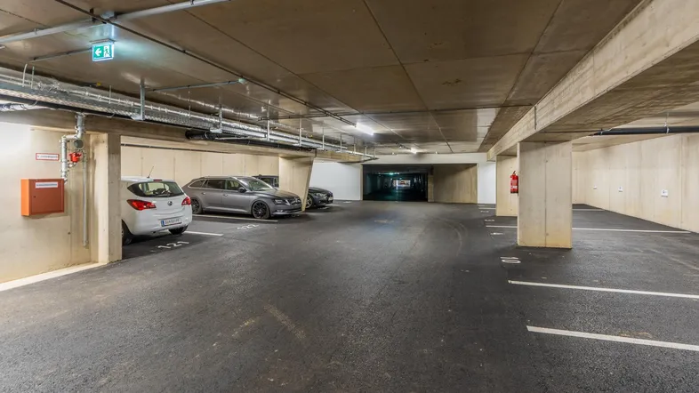 Geräumige Tiefgarage mit mehreren Stellplätzen und sichtbaren Installationen an der Decke.
