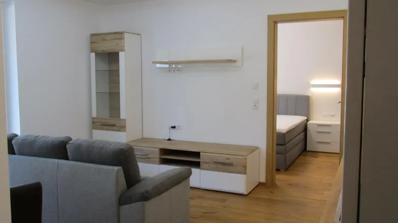 Heller Wohnbereich mit Sofa, Mediamöbeln und Blick auf das angrenzende Schlafzimmer.