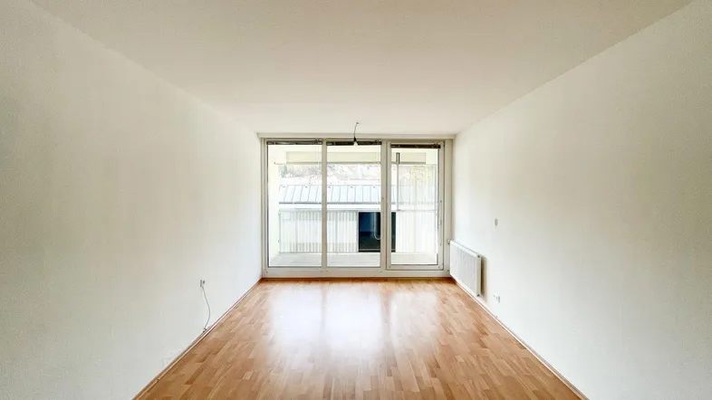 Helles Zimmer mit Parkettboden und großem Fenster, das Zugang zu einem Balkon bietet.