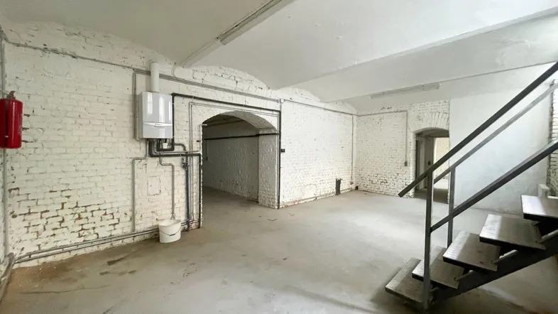 Geräumiger Kellerraum mit weiß gestrichenen Ziegelwänden, Betonboden und sichtbarer Heizungsanlage.