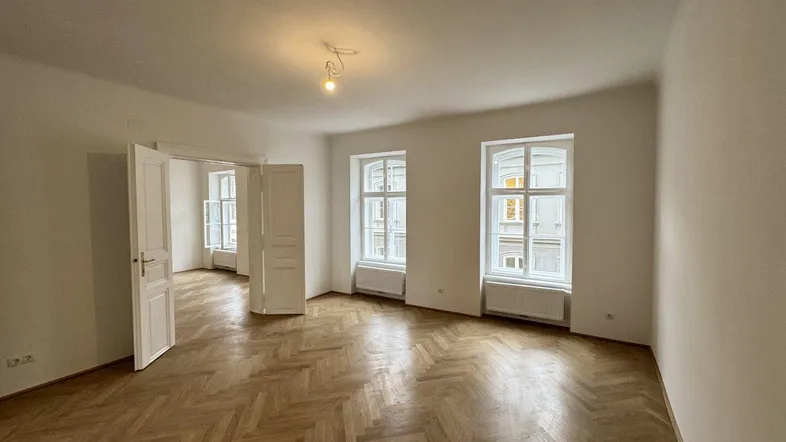 Helles Zimmer mit Fischgrätparkett und hohen Fenstern, das vielseitig nutzbar ist.
