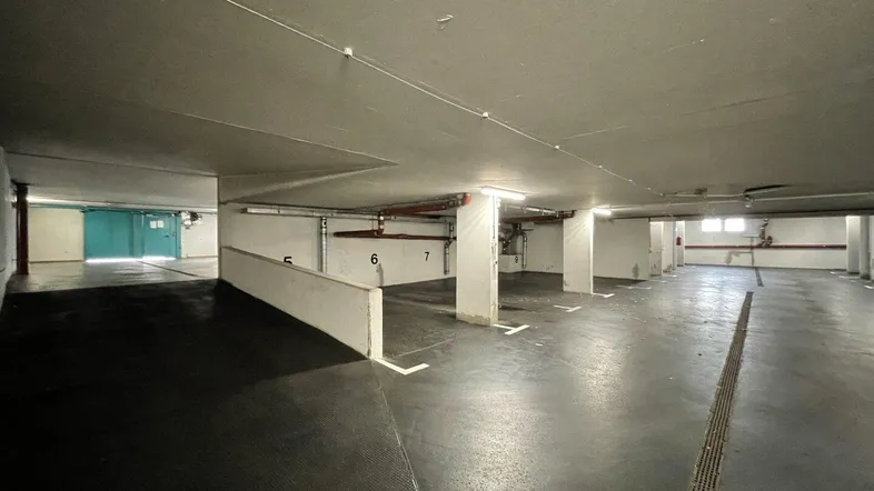 Geräumige Tiefgarage mit mehreren nummerierten Stellplätzen und hellen Leuchtstoffröhren an der Decke.