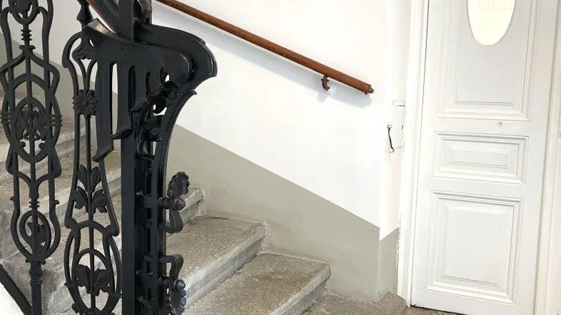 Historisches Treppenhaus mit kunstvollem schmiedeeisernem Geländer und gemusterten Fliesenboden.